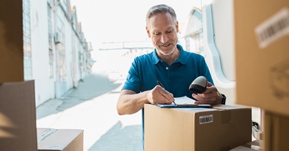 mature delivery man signing checklist on pile of boxes