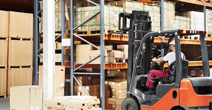 warehouse worker driver in uniform loading cardboxes by forklift stacker loader