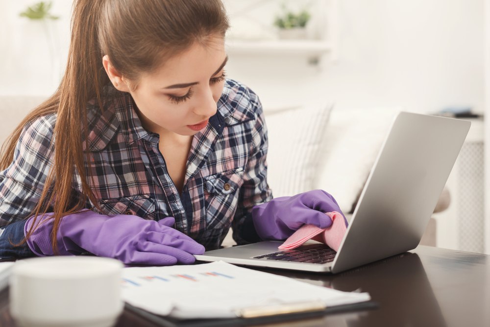 woman wearing rubber gloves and wiping down laptop
