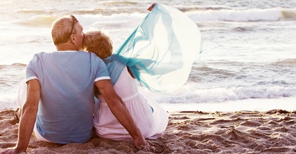 mature retired couple sitting in the sand by the ocean