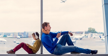 Father and son looking at their phones while sitting in window at airport