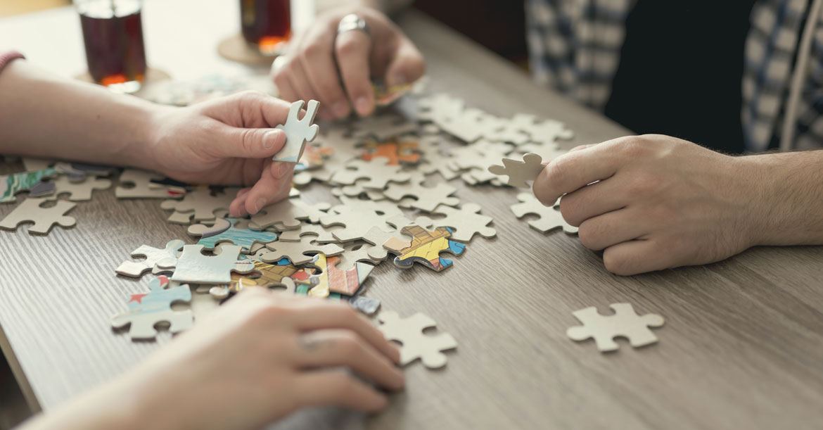 Close up of two sets of hands sorting through colorful puzzle pieces laying on wood table.