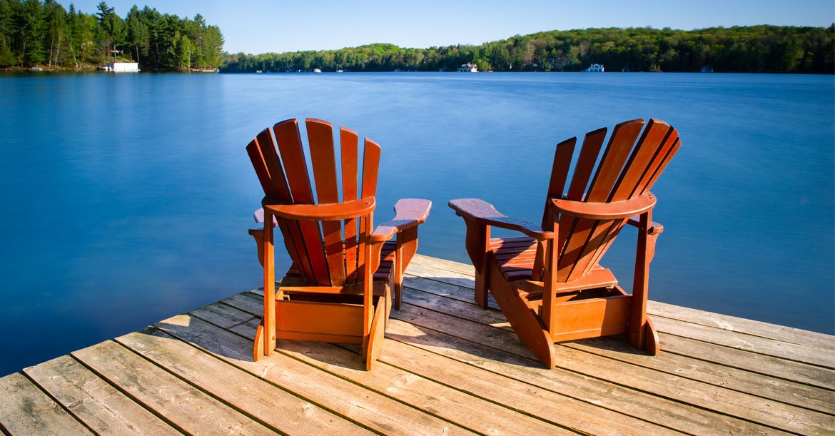 two empty adirondack chairs sitting on dock by water