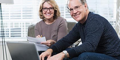 smiling mature couple sitting on couch while working on computer