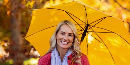 smiling woman holding yellow umbrella in the fall
