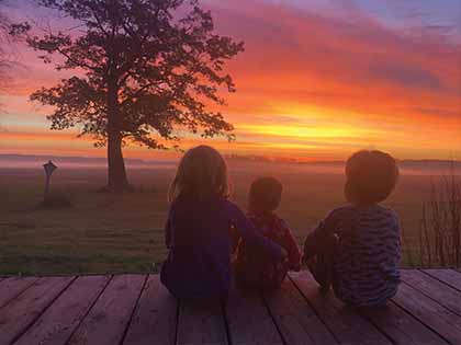 three small children look out at orange, yellow, and pink sunrise