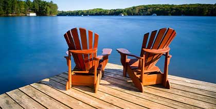 two empty adirondack chairs sitting at end of dock overlooking blue lake