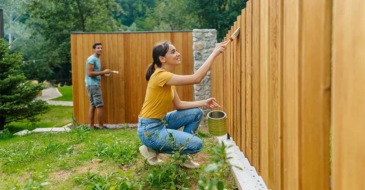 couple painting fence on new home
