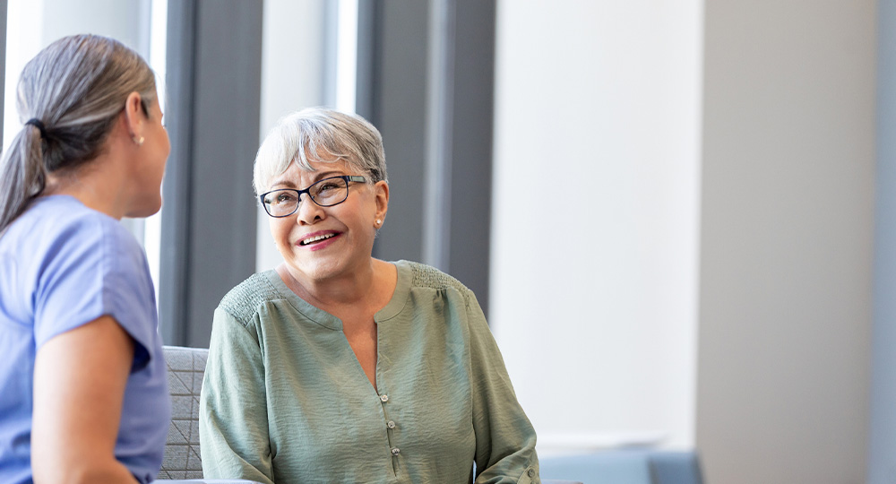 Senior woman in a clinic while a healthcare provider offers care, representing the type of services commonly covered by Medicare.