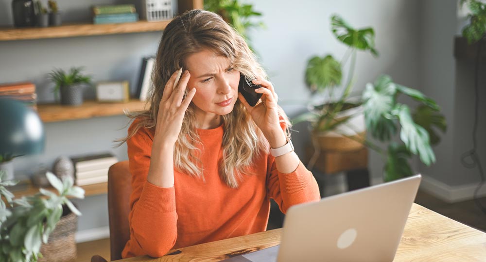 Worried small business owner on the phone while checking a laptop, concerned about a possible impersonation scam or fraud attempt.