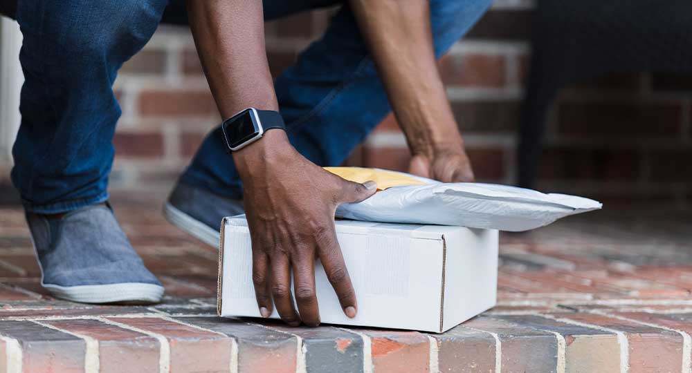 Person picking up unsolicited package on doorstep that may be brushing fraud.