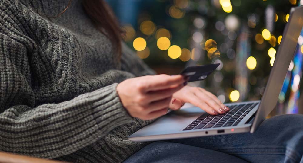 Online shopping with a credit card near holiday decorations, illustrating potential holiday scams and fraud.