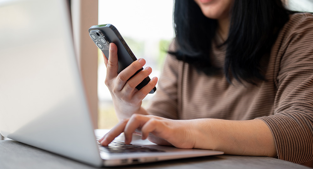 Woman setting up mobile banking alerts with laptop and phone.
